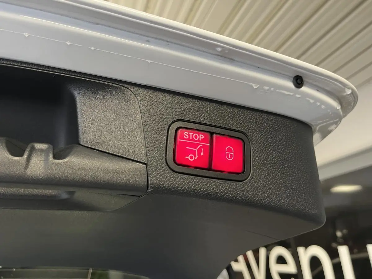 Boutons rouges de fermeture électrique du hayon sur le coffre d'un break Mercedes Classe C blanc.