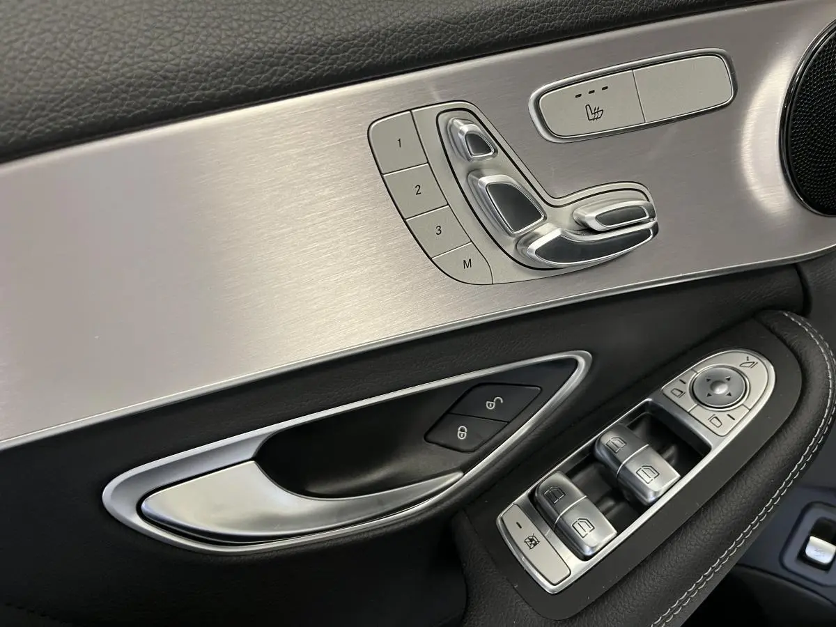 Détail de la porte côté conducteur d'une Mercedes Classe C Break blanc, avec commandes sièges et vitres en finition aluminium brossé.
