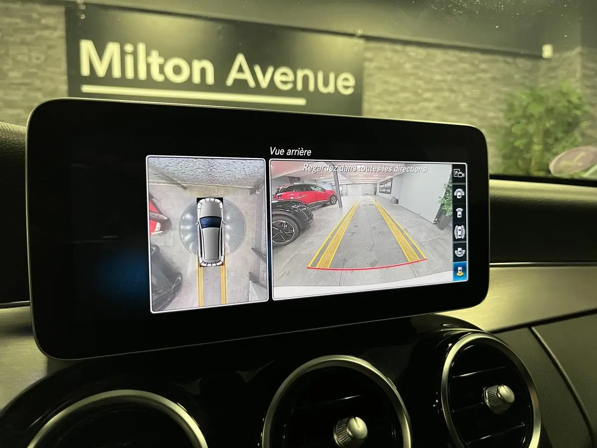Écran multimédia montrant la caméra de recul et vue 360° d'un break Mercedes Classe C blanc, intérieur noir.