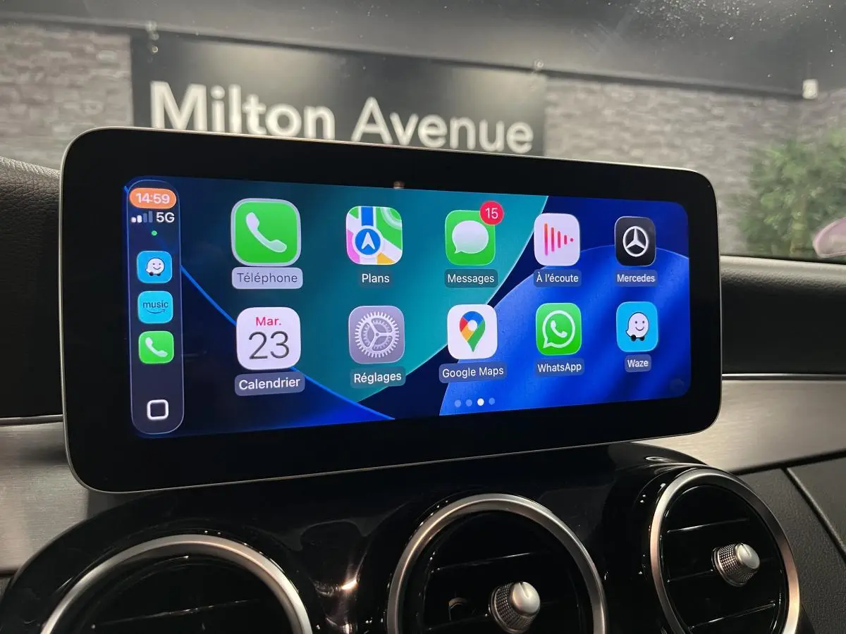 Écran tactile central affichant l’intégration smartphone dans le tableau de bord noir d’un Mercedes Classe C Break blanc.
