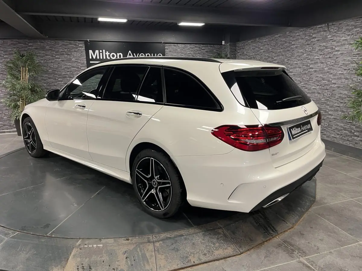 Vue 3/4 arrière côté gauche d'un break Mercedes Classe C blanc avec jantes AMG noires et vitres teintées.