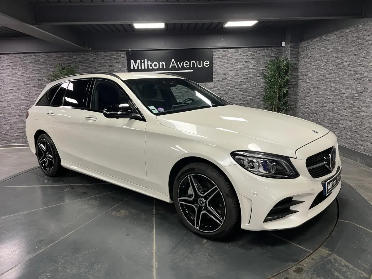 Mercedes Classe C Break blanc en 3/4 avant droit avec jantes AMG noires et toit ouvrant visible en intérieur showroom.