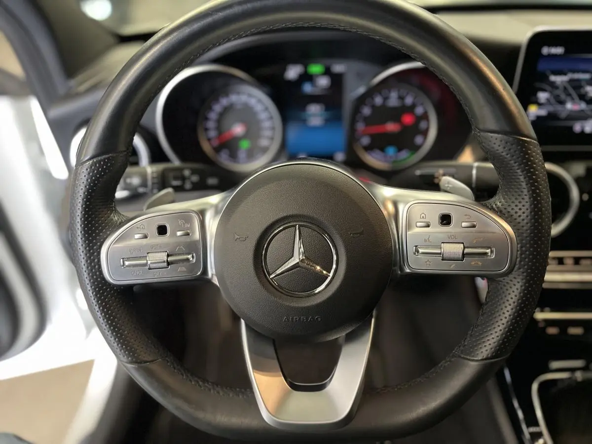 Volant sport en cuir noir avec commandes intégrées dans une Mercedes Classe C Break blanc, vue rapprochée frontale.