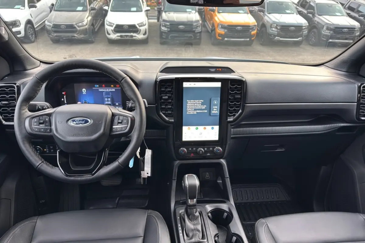 Vue intérieure du Ford Ranger 2025 montrant le tableau de bord noir avec écran tactile vertical et volant multifonctions.
