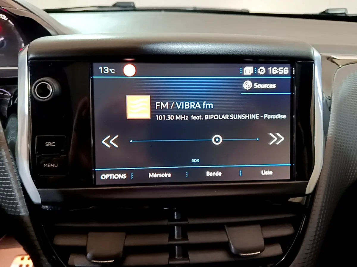 Écran tactile central affichant la radio FM dans l’habitacle d’une Peugeot 2008 gris foncé, vue de face rapprochée.