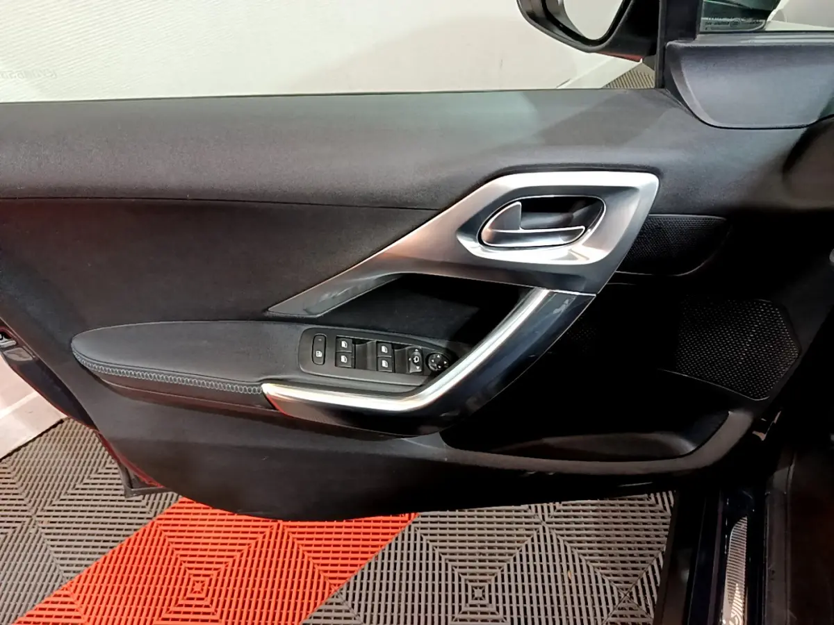 Vue intérieure du panneau de porte côté conducteur du Peugeot 2008 gris foncé, avec commandes électriques et poignée argentée.