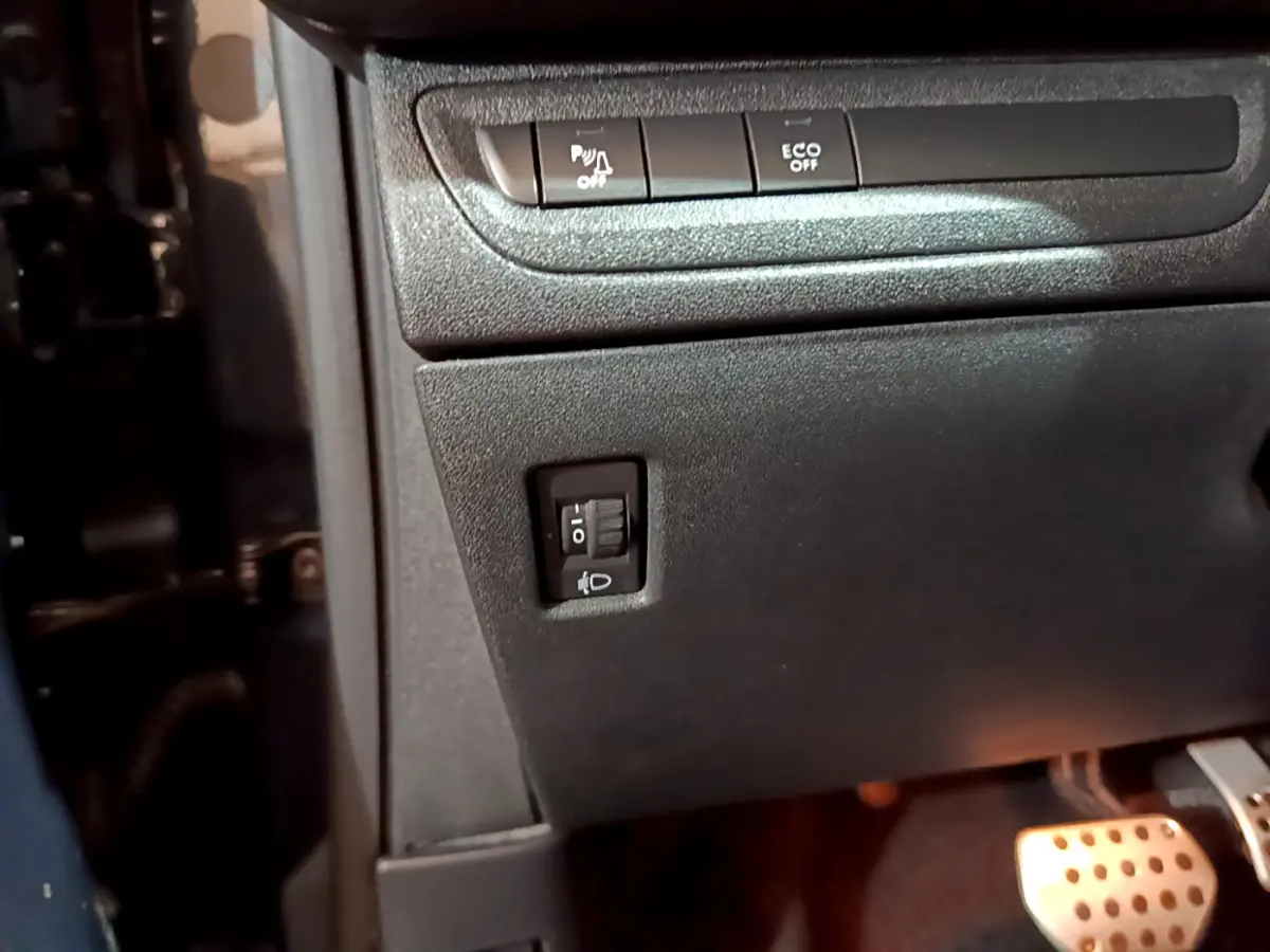 Détail du tableau de bord côté gauche avec boutons de réglage des phares et pédales en aluminium du Peugeot 2008 gris foncé.