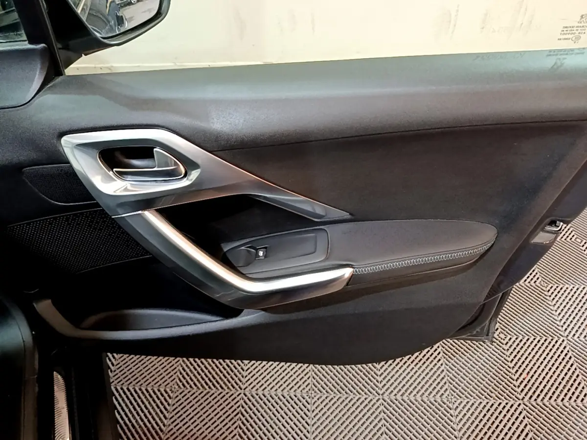 Gros plan sur la porte intérieure côté gauche du Peugeot 2008 gris foncé, avec poignée argentée et accoudoir noir.