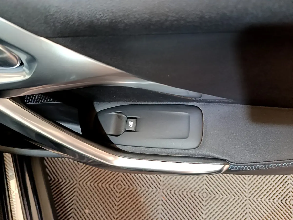 Détail de la commande d'ouverture de coffre sur la porte intérieure côté gauche d'un Peugeot 2008 gris foncé.