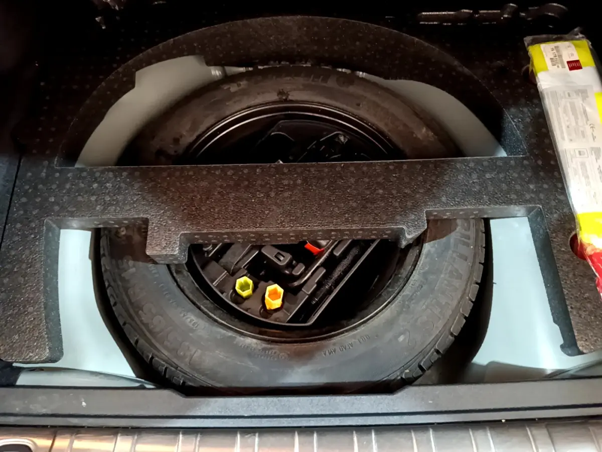 Vue plongeante sur la roue de secours noire et les outils de bord dans le coffre d'un Peugeot 2008 gris foncé.