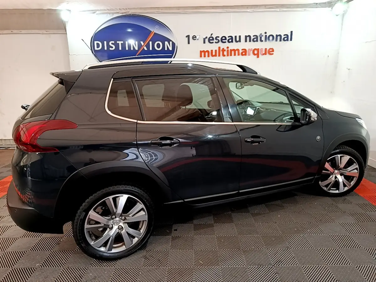 Peugeot 2008 gris foncé vue de profil côté gauche, avec jantes alliage et barres de toit chromées.