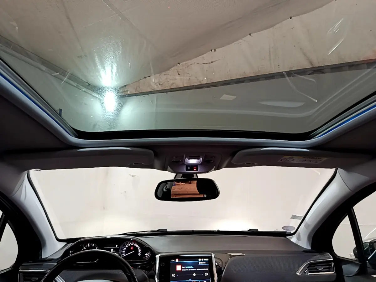 Vue intérieure avant du Peugeot 2008 gris foncé 2019, avec toit panoramique et tableau de bord tactile allumé.