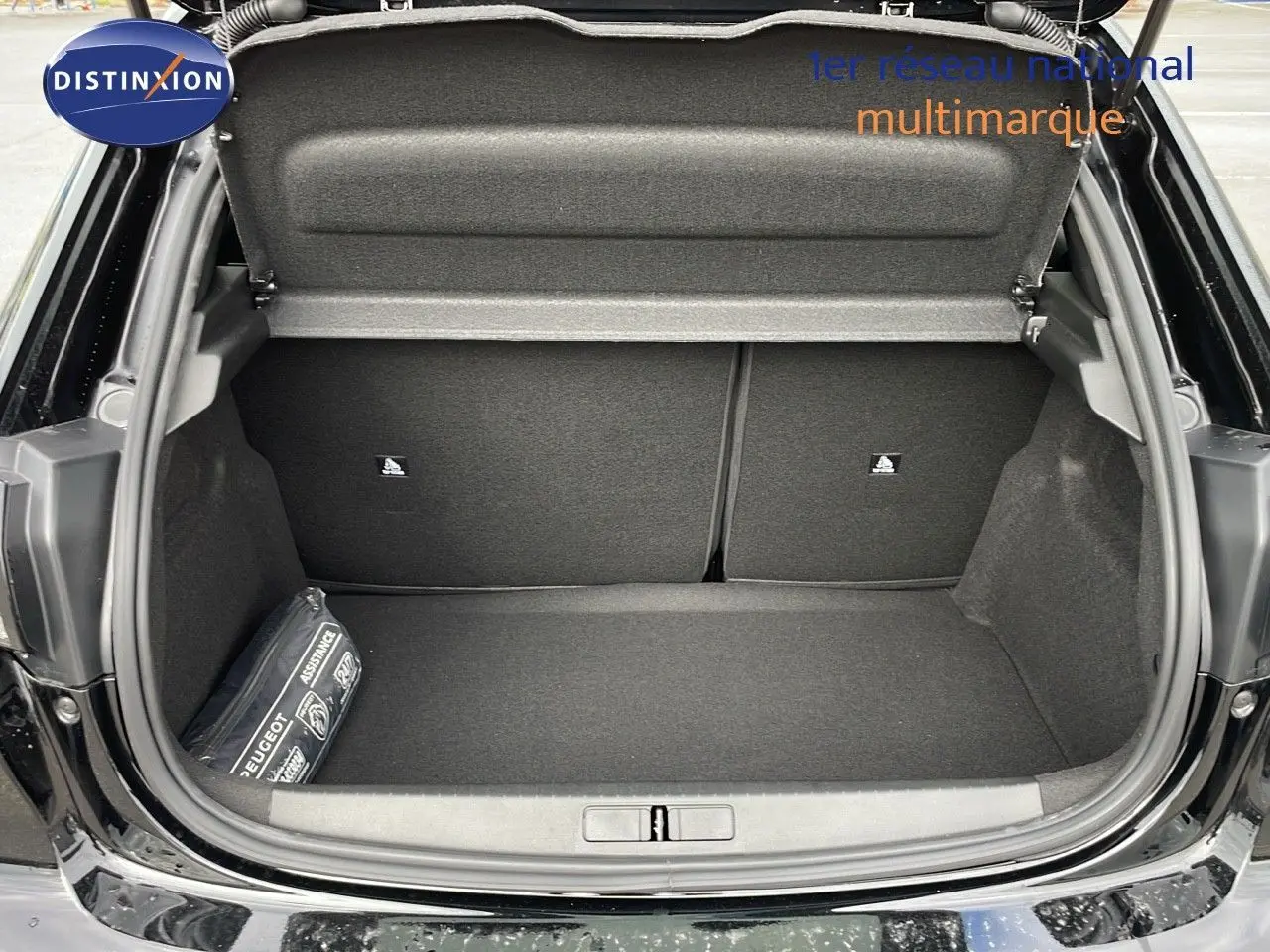 Coffre ouvert d'une Peugeot 208 noir perla metal, montrant un espace de rangement propre et un kit d'assistance sur le côté gauche.