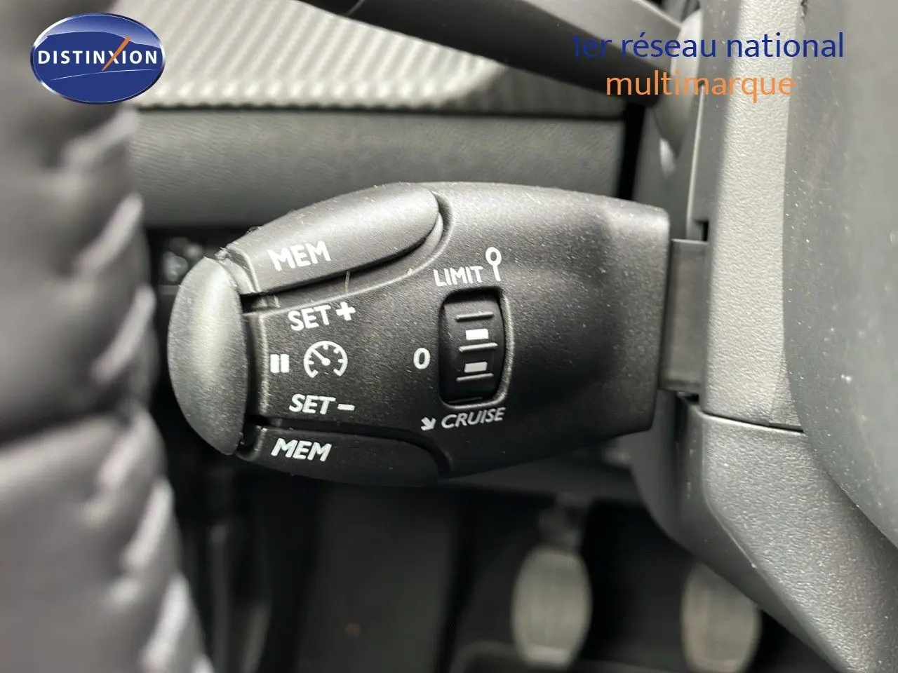 Gros plan sur la commande de régulateur de vitesse à gauche du volant dans une Peugeot 208 noire Perla Metal 2024.