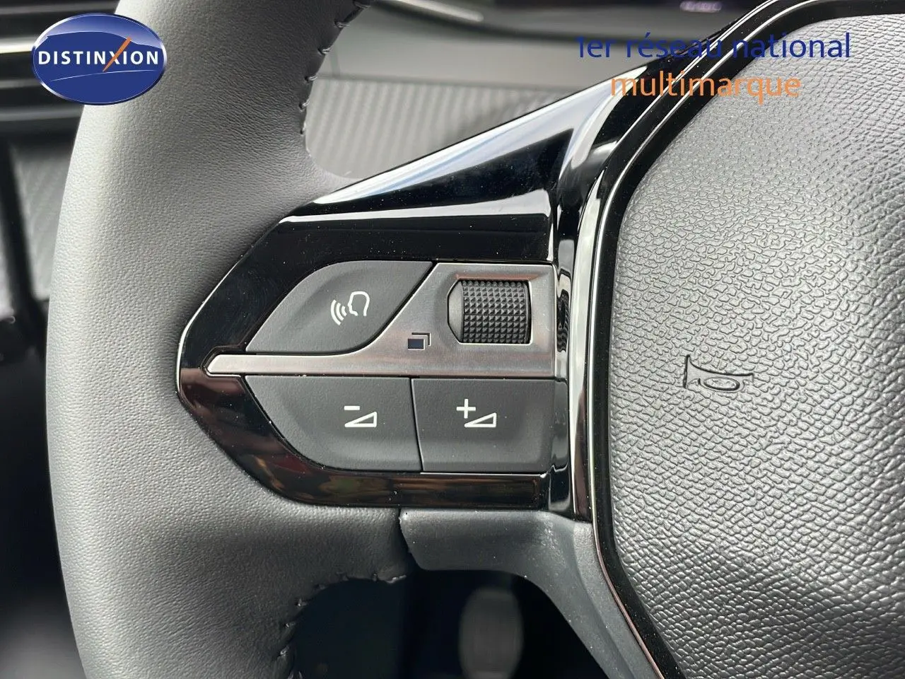 Gros plan sur les commandes du volant de la Peugeot 208 noire, mettant en valeur les boutons de volume et de téléphone.