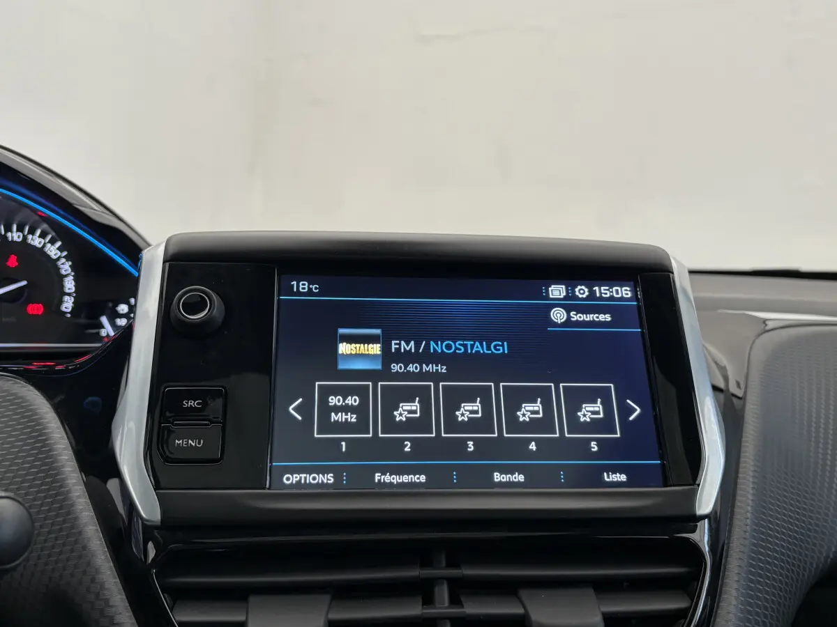 Vue rapprochée de l'écran tactile multimédia du Peugeot 2008 rouge, affichant la radio FM sur fond noir et bleu.