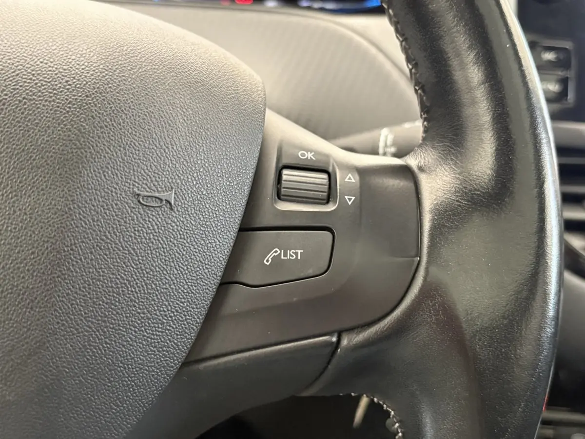 Gros plan sur le volant cuir noir de la Peugeot 2008 Puretech 110, avec commandes multifonctions côté droit.