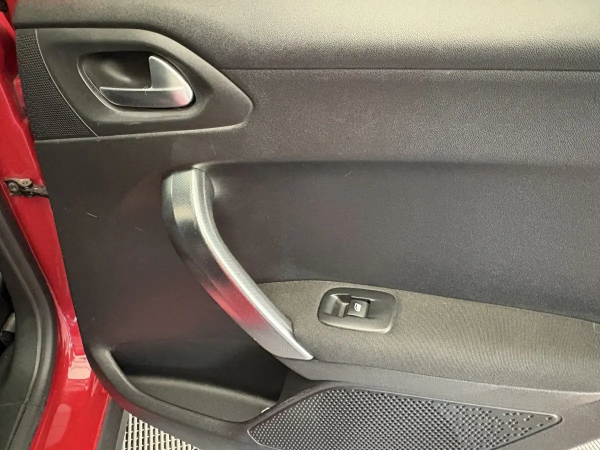 Gros plan sur la porte intérieure côté gauche d'une Peugeot 2008 rouge, avec poignée argentée et bouton de vitre électrique.