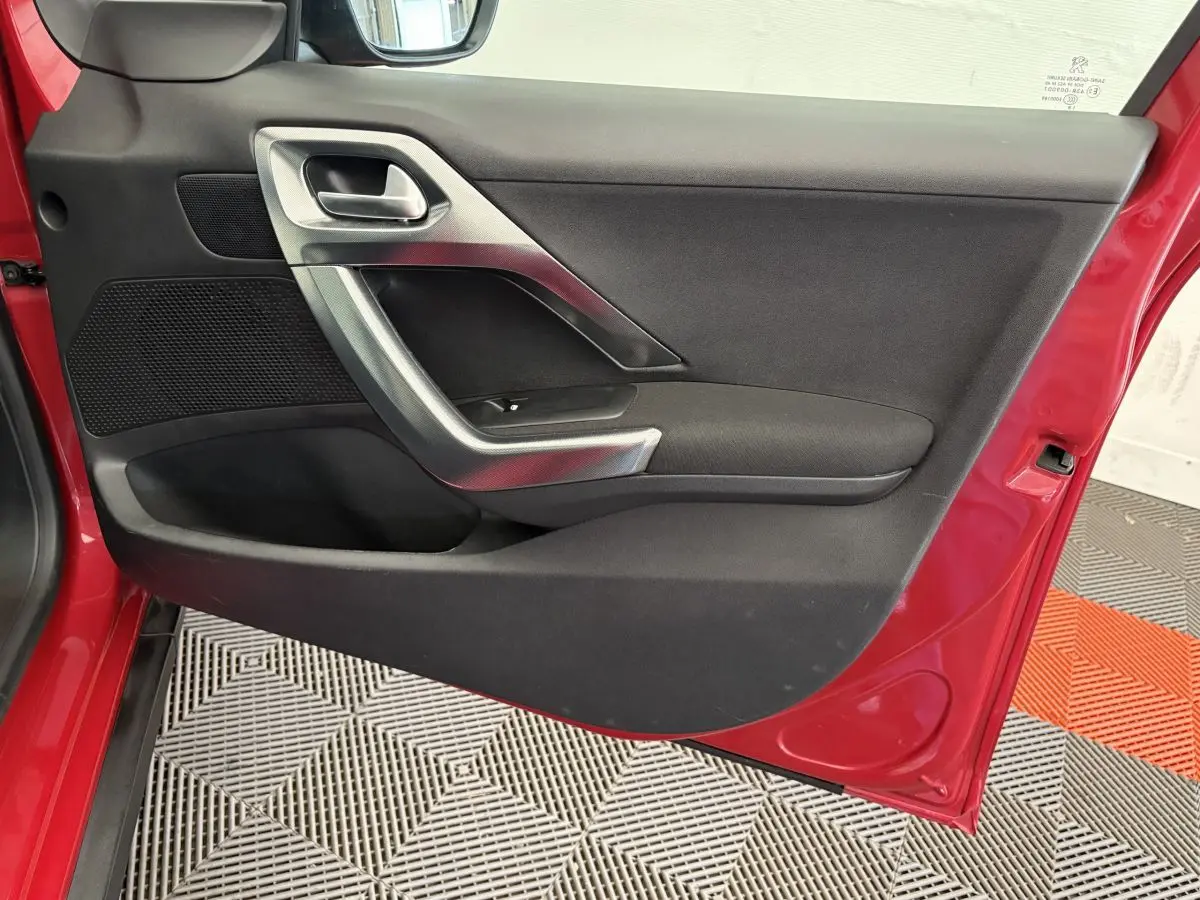 Vue rapprochée de la porte avant gauche rouge d'un Peugeot 2008 2019, avec poignée argentée et panneau noir.