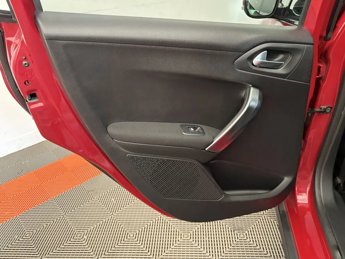Vue rapprochée de la porte arrière gauche rouge du Peugeot 2008 avec poignée argentée et panneau noir intérieur.