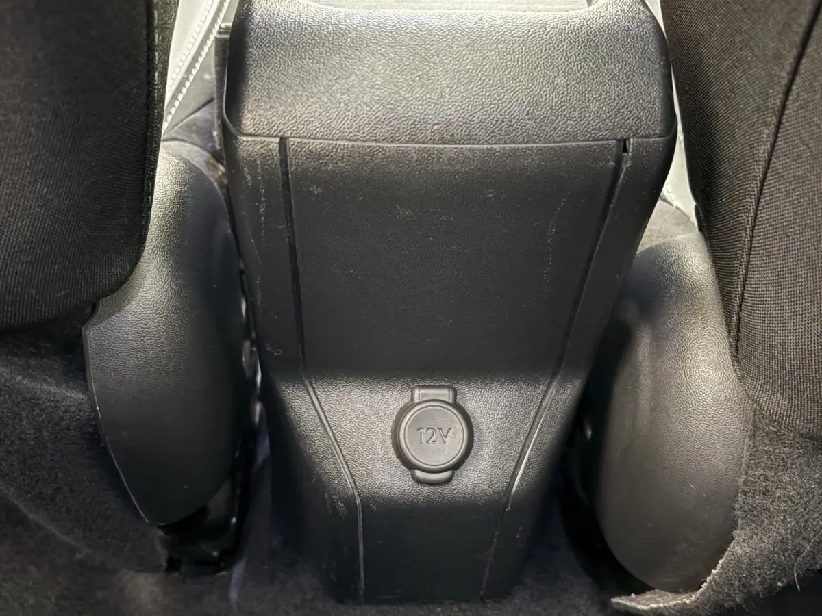 Prise 12V en gros plan entre les sièges arrière noirs d'une Peugeot 2008 rouge, version Puretech 110 S&S EAT6 Allure.