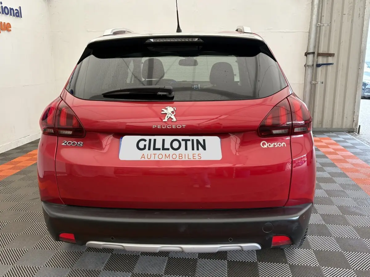 Vue arrière d'un Peugeot 2008 rouge avec logo et feux arrière distinctifs, stationné en intérieur sur sol damier.