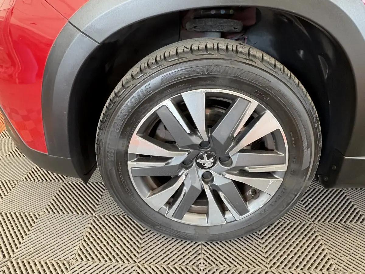 Gros plan sur la roue avant gauche du Peugeot 2008 rouge, mettant en valeur la jante alliage et le logo lion central.