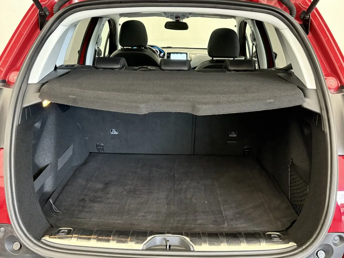 Coffre ouvert d'un Peugeot 2008 rouge vu de l'arrière, avec tablette cache-bagages et intérieur noir visible.