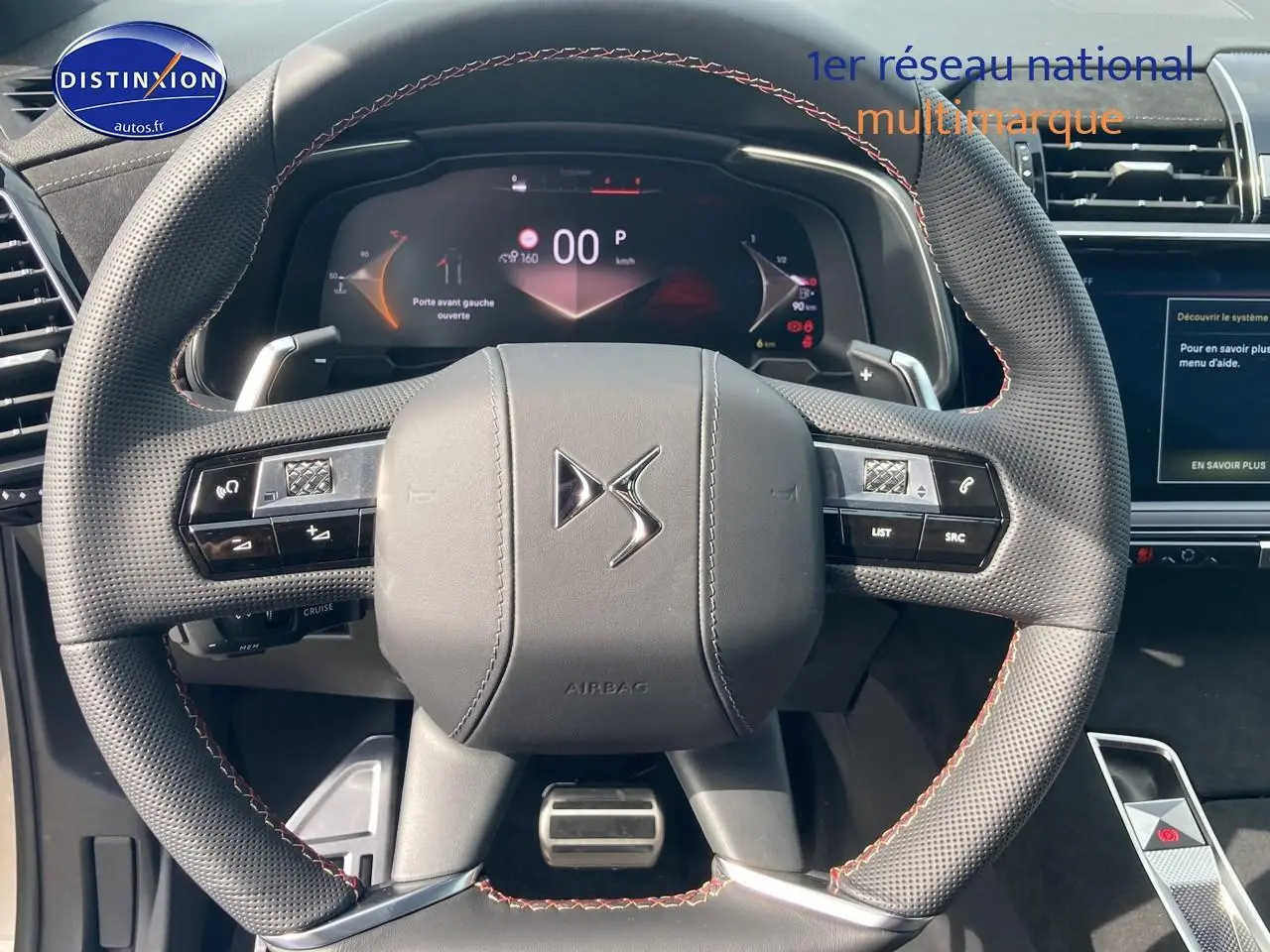 Vue rapprochée du volant cuir perforé avec surpiqûres rouges du DS7 1.5 BlueHDi 130 Performance Line, tableau de bord digital visible.