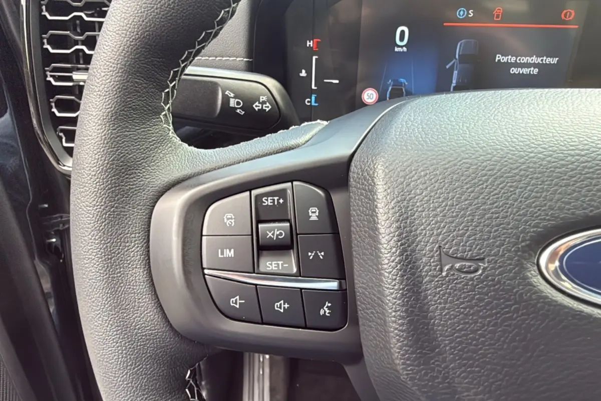 Gros plan sur le volant cuir noir du Ford Ranger 2025, avec commandes multifonctions et tableau de bord digital en arrière-plan.