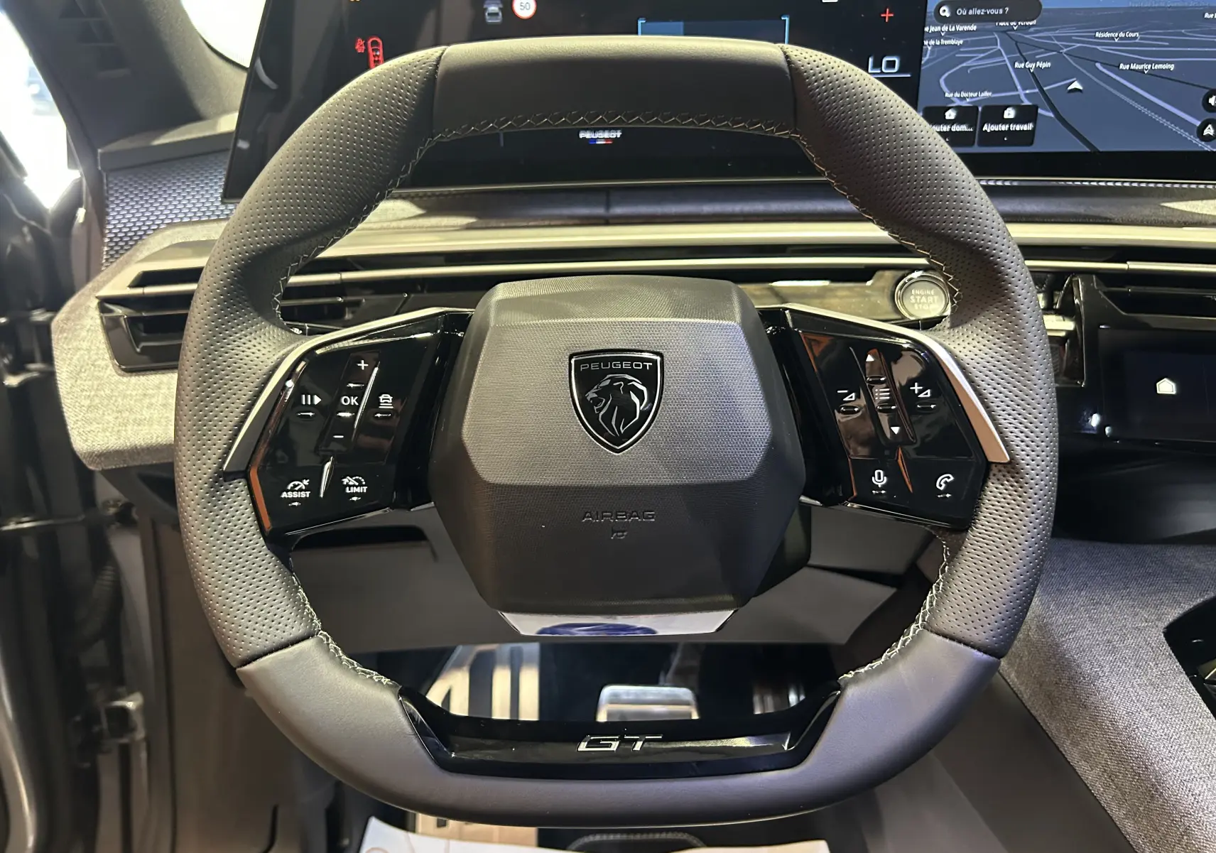 Vue rapprochée du volant cuir gris perforé du Peugeot 3008 Hybrid GT avec commandes intégrées et logo GT au bas.