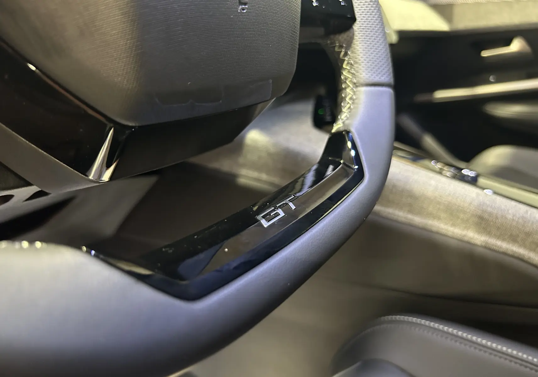 Gros plan sur le volant cuir noir avec logo GT du Peugeot 3008 III Hybrid, intérieur moderne et soigné.