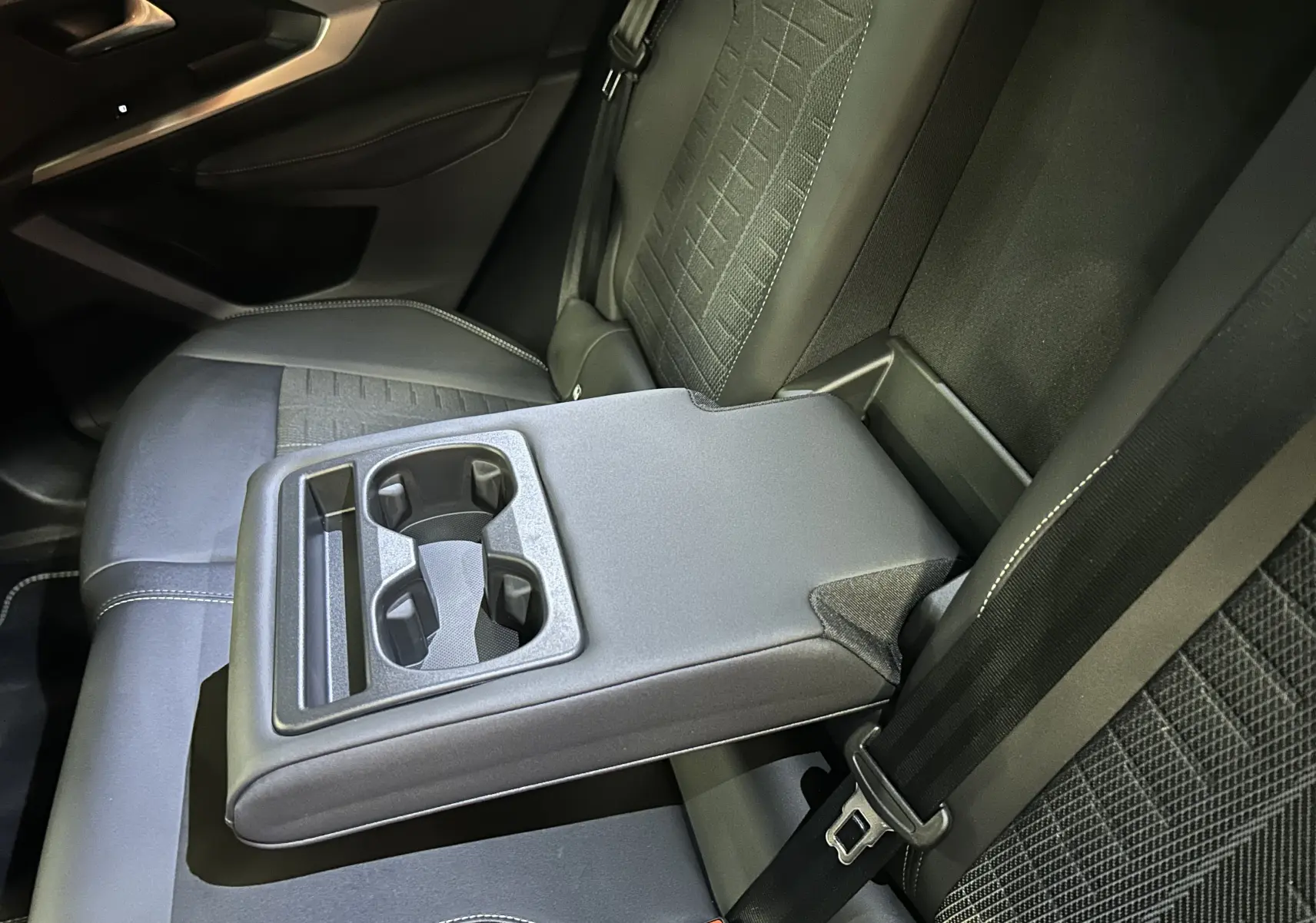 Vue rapprochée de l’accoudoir central arrière avec porte-gobelets sur les sièges noirs du Peugeot 3008 Hybrid 2026.