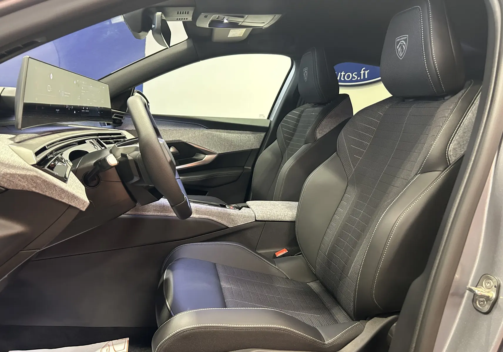 Vue intérieure côté conducteur du Peugeot 3008 Hybrid gris Artense, sièges en cuir noir avec logo Peugeot brodé sur les appuie-têtes.