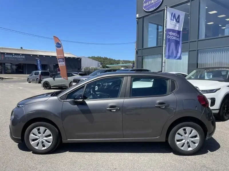 Profil côté gauche d'une Citroën C3 2019 gris foncé métal, version 82 CV FEEL, stationnée devant un concessionnaire.