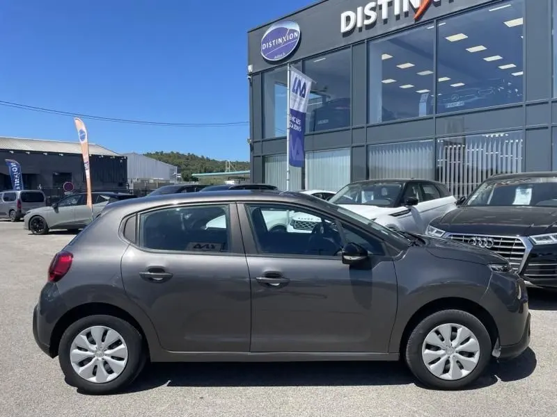 Profil côté gauche d'une Citroën C3 2019 gris foncé métal, version 82 CV Feel, stationnée devant un concessionnaire.