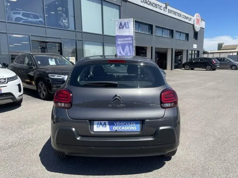 Vue arrière d'une Citroën C3 82 CV Feel gris foncé métal de 2019, stationnée devant un garage de véhicules d'occasion.