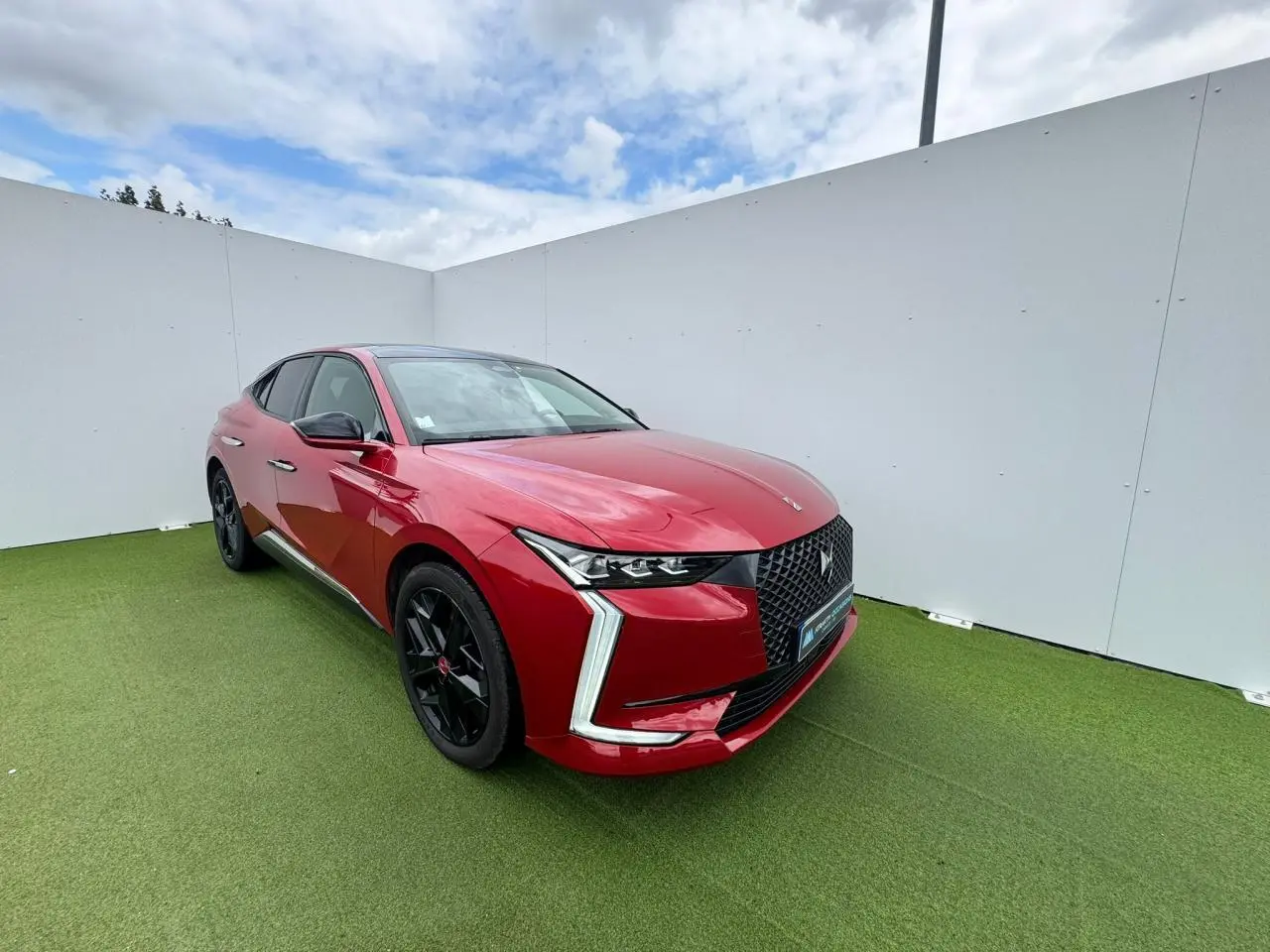 Vue 3/4 avant d'une DS4 rouge foncé avec calandre noire et jantes alliage noires sur fond vert gazon.
