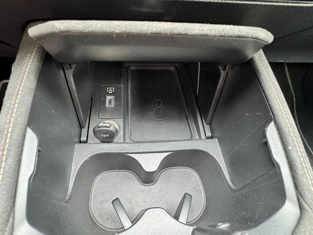 Gros plan sur la console centrale noire du DS4 II avec porte-gobelets, prise 12V et chargeur sans fil intégré.