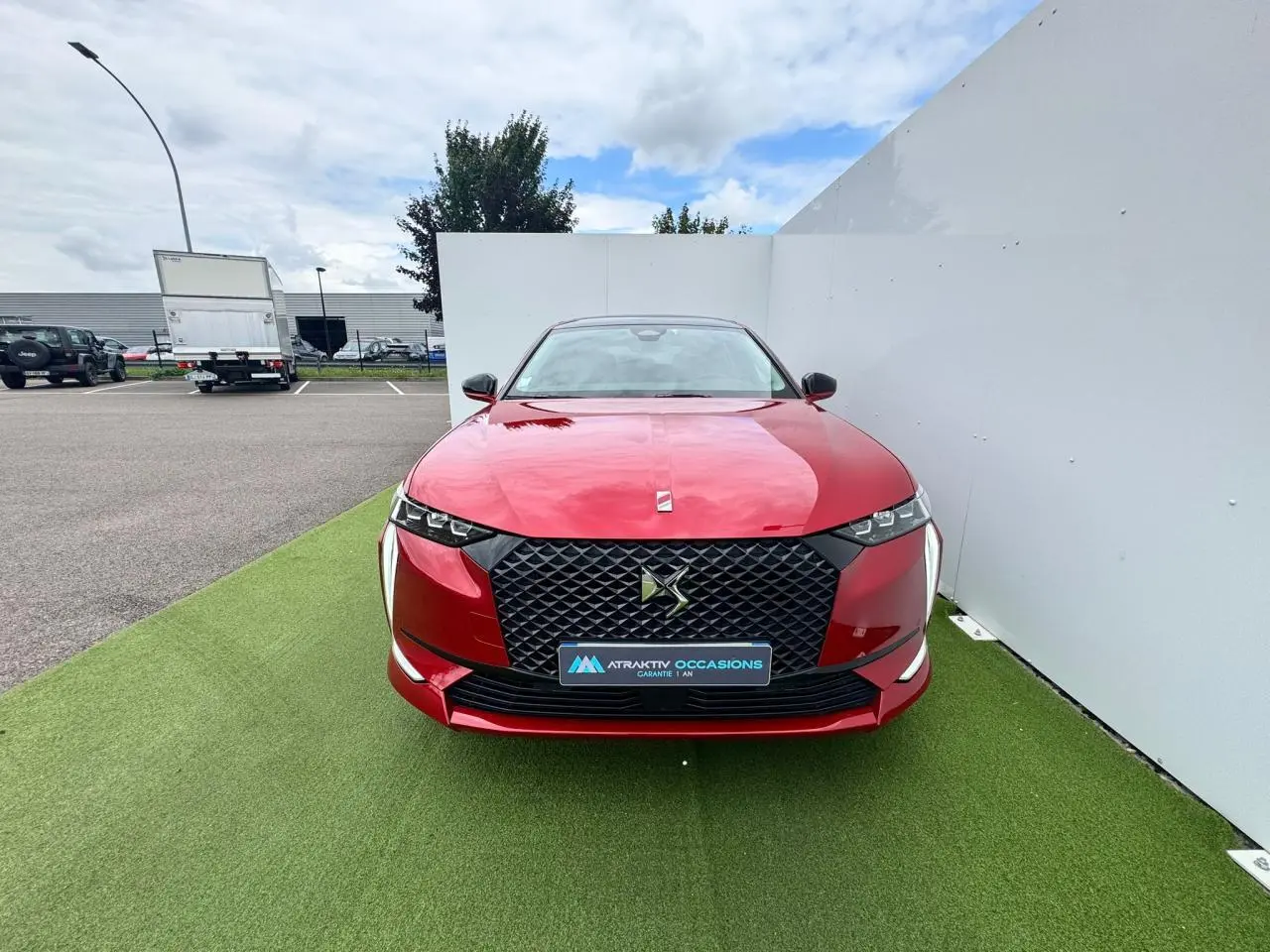 Vue frontale d'une DS4 rouge foncé avec calandre noire et feux LED distinctifs sur fond extérieur neutre.