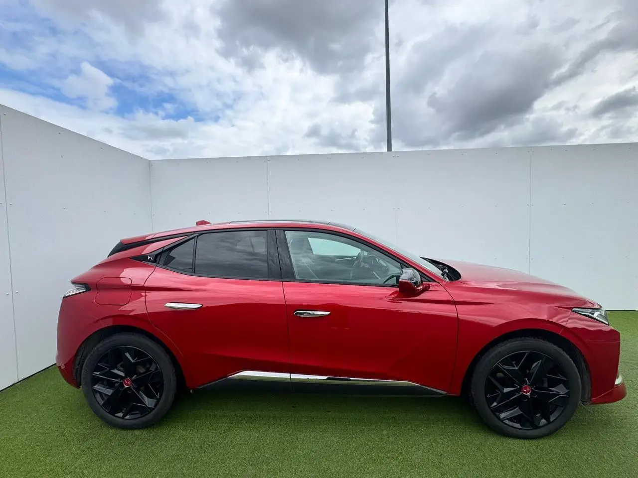 Profil côté gauche d'une DS4 rouge foncé avec jantes noires et toit panoramique sous un ciel nuageux.