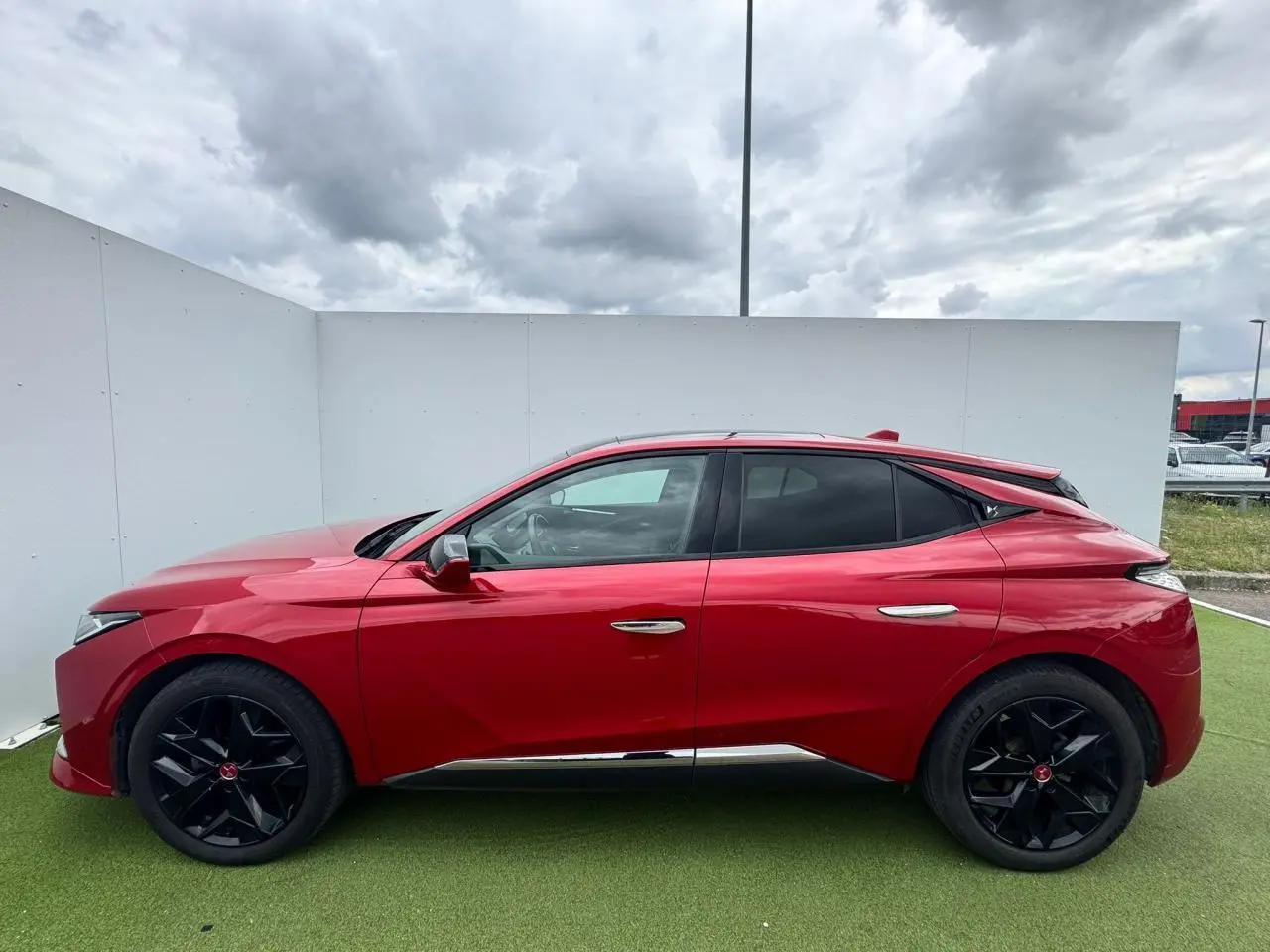 Vue latérale gauche d'une DS4 rouge foncé avec jantes noires et détails chromés sous un ciel nuageux.