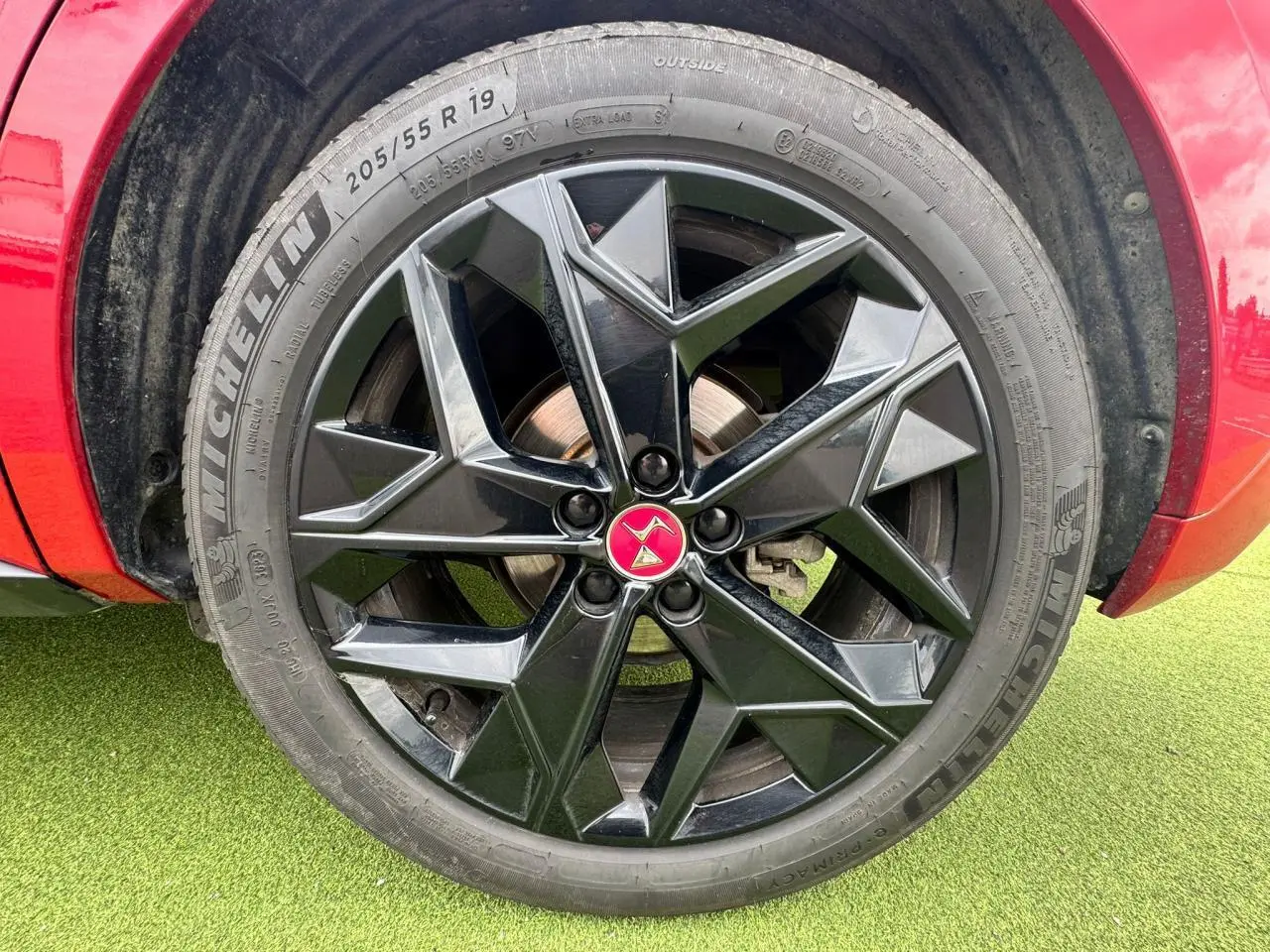Gros plan sur la jante noire brillante 19 pouces avec logo DS rouge du DS4 rouge foncé, côté gauche avant.