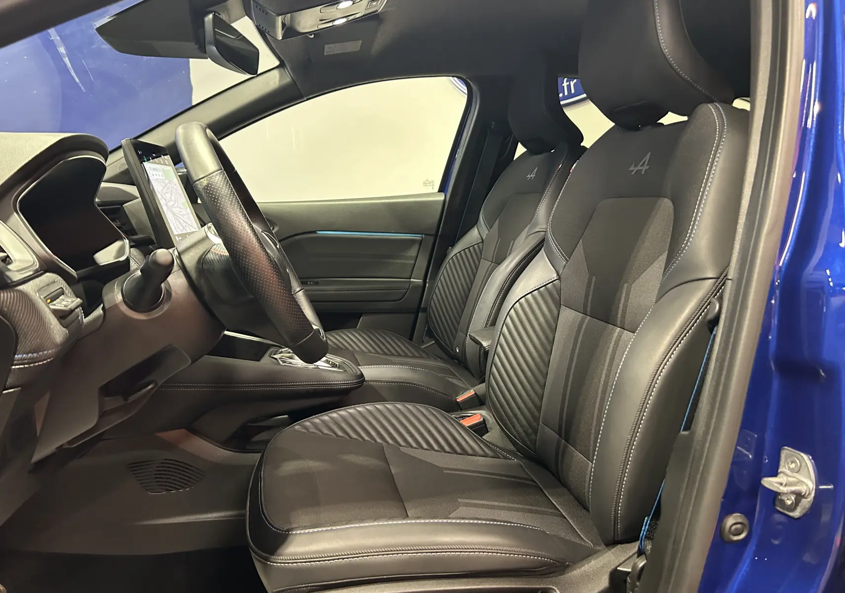 Vue intérieure côté conducteur du Renault Captur bleu Iron 2025, sièges noirs avec logo Alpine brodé.