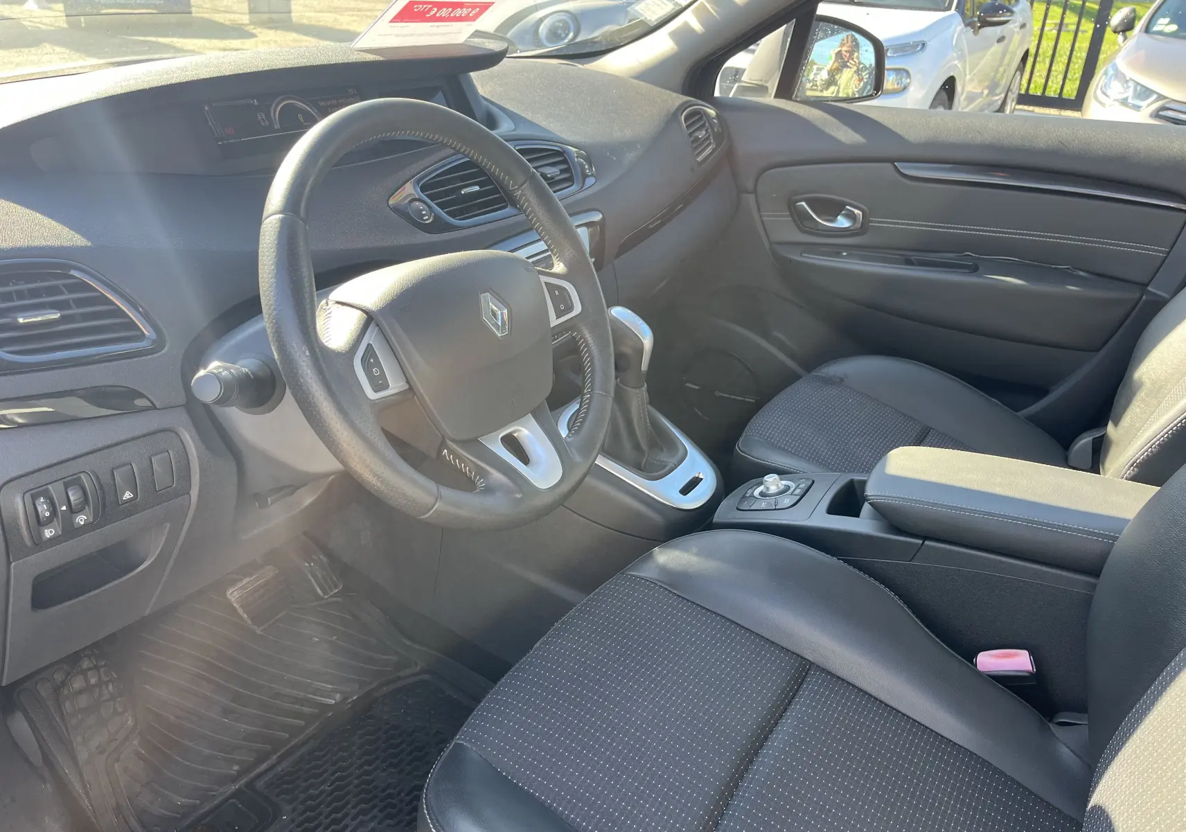 Vue intérieure côté conducteur du Renault Scenic III noir de 2012, volant cuir et console centrale avec boîte automatique.