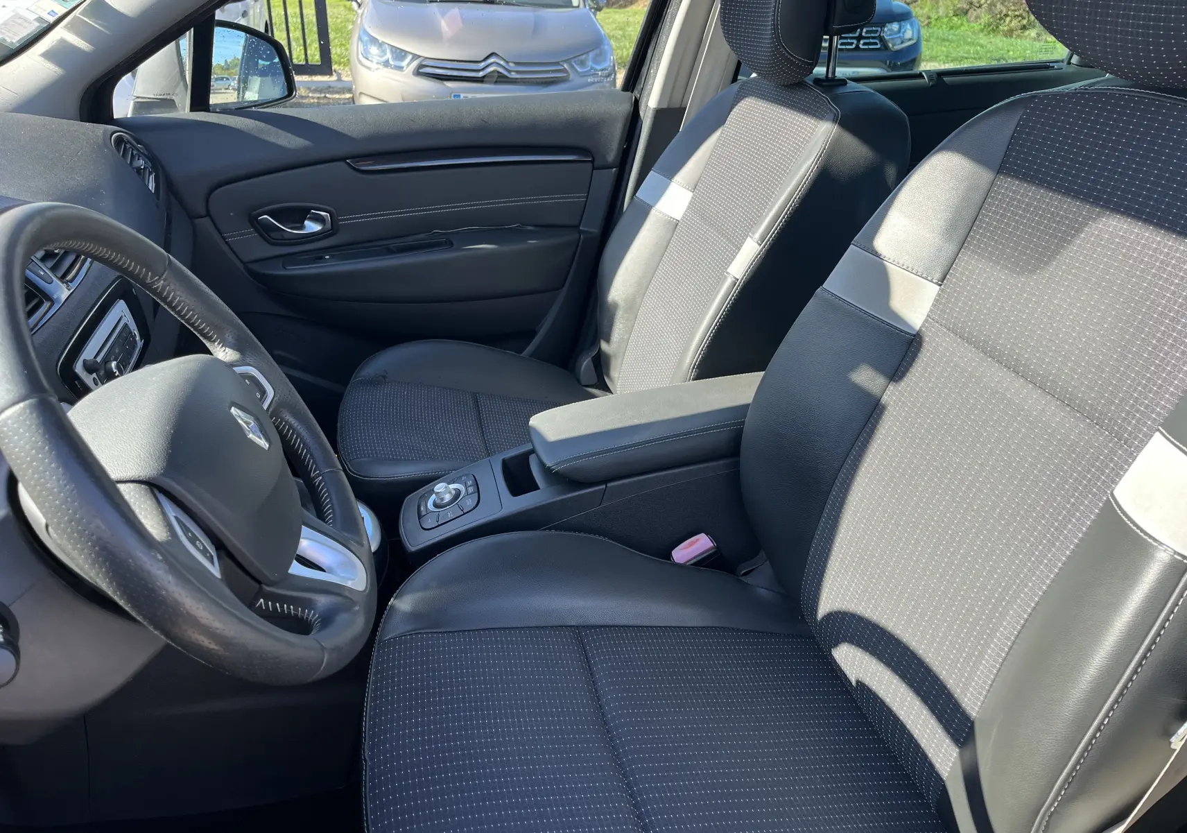 Intérieur de Renault Scénic III 2012 en vue latérale gauche, sièges tissu et cuir noir avec console centrale et volant visible.