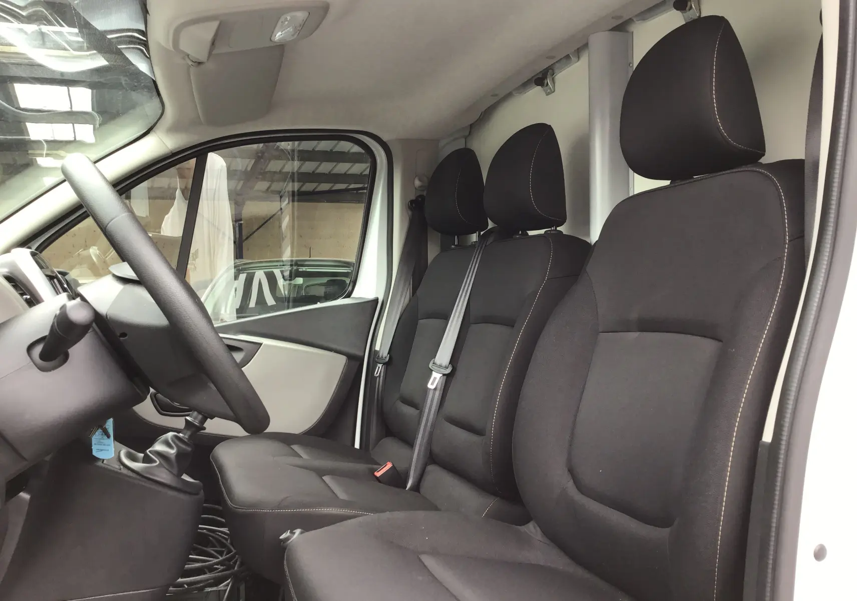 Vue intérieure côté conducteur du Renault Trafic Planche cabine blanc 2019, sièges noirs et volant visible.