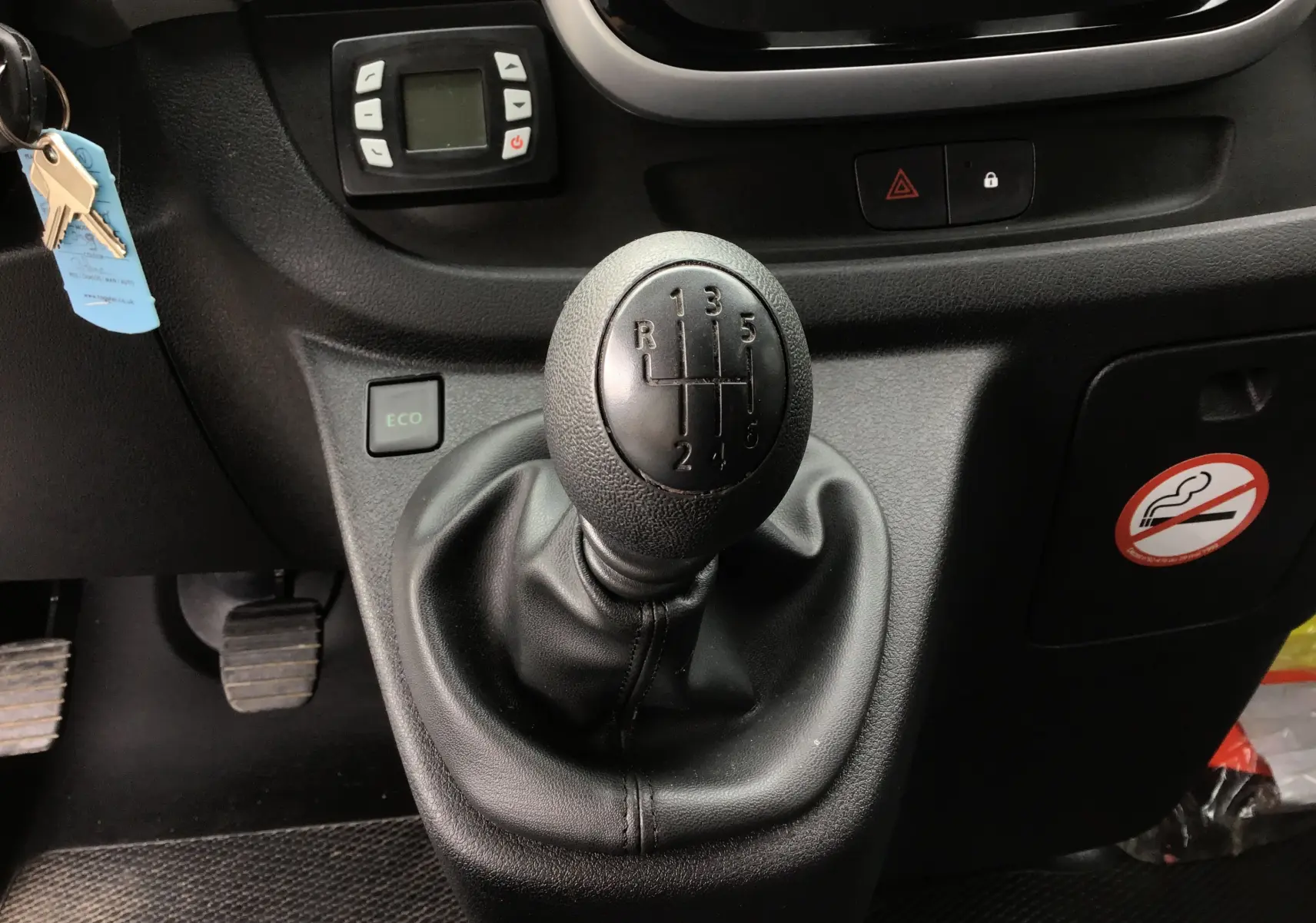 Gros plan sur le levier de vitesses manuelle noir du Renault Trafic Planche cabine blanc, avec bouton ECO et pédales visibles.