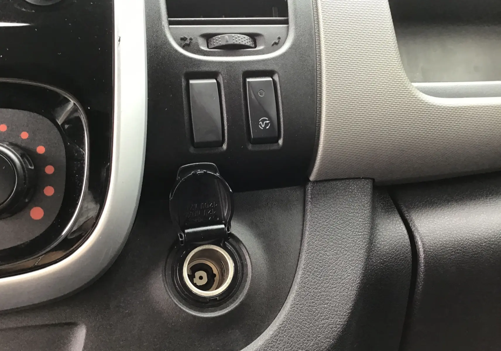 Prise allume-cigare ouverte sur le tableau de bord noir et gris du Renault Trafic Planche cabine blanc, version frigorifique.