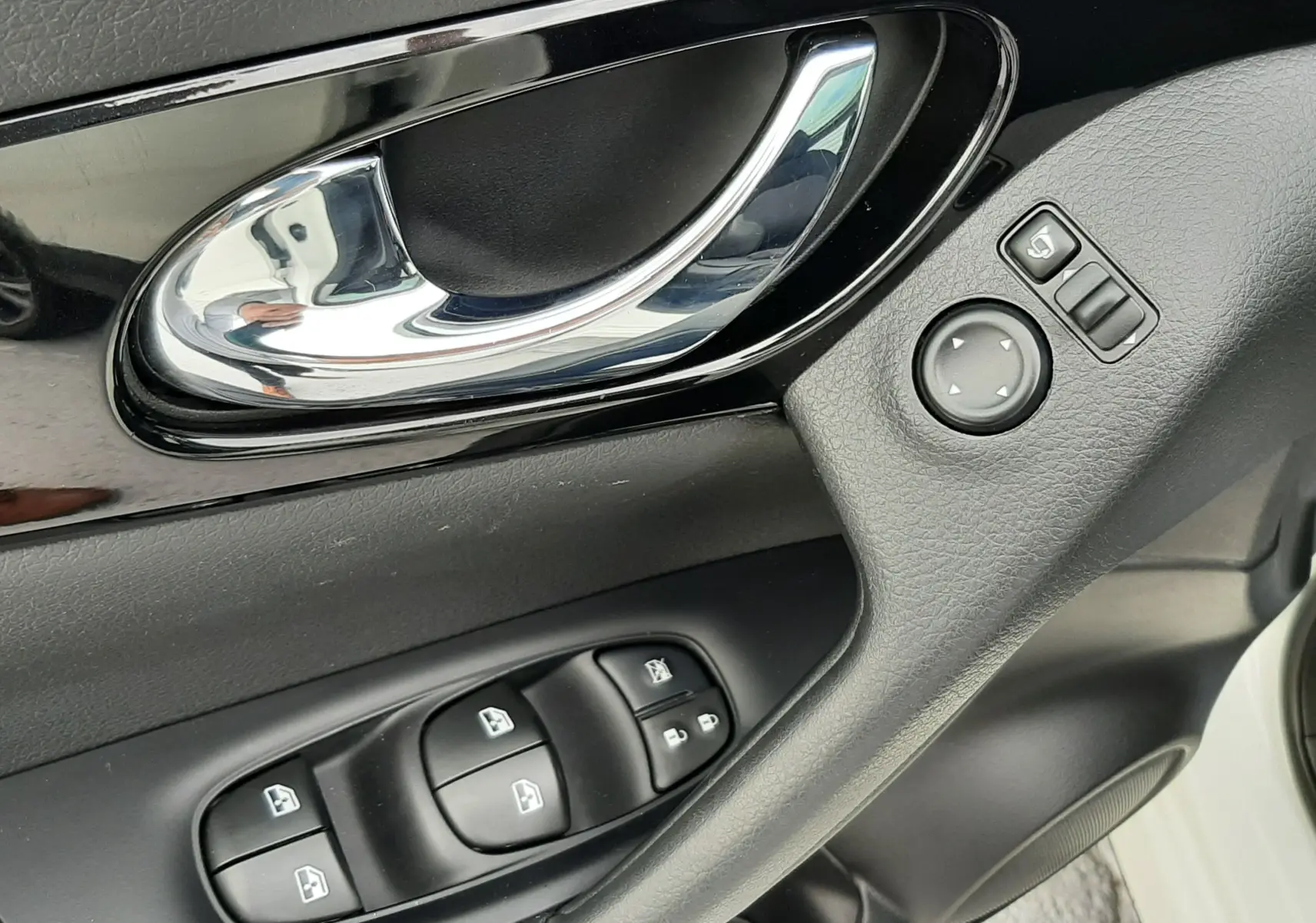Poignée de porte intérieure côté conducteur du Nissan Qashqai blanc 2020 avec commandes des vitres et réglages des rétroviseurs.